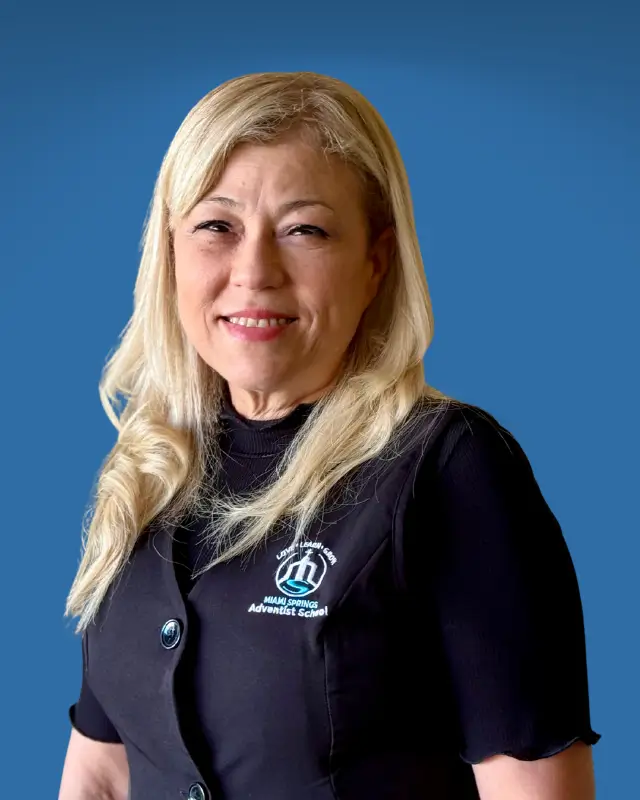 Smiling blonde woman in a black vest with a school logo against a blue background.