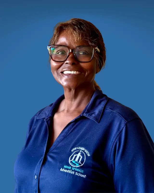 Smiling African American woman wearing a blue polo shirt with a school logo on the left, posed against a solid blue background.