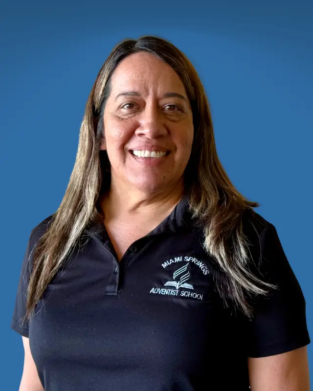 Portrait of a smiling woman with long brown hair, wearing a black polo shirt with the Miami Springs Adventist School logo against a blue background.